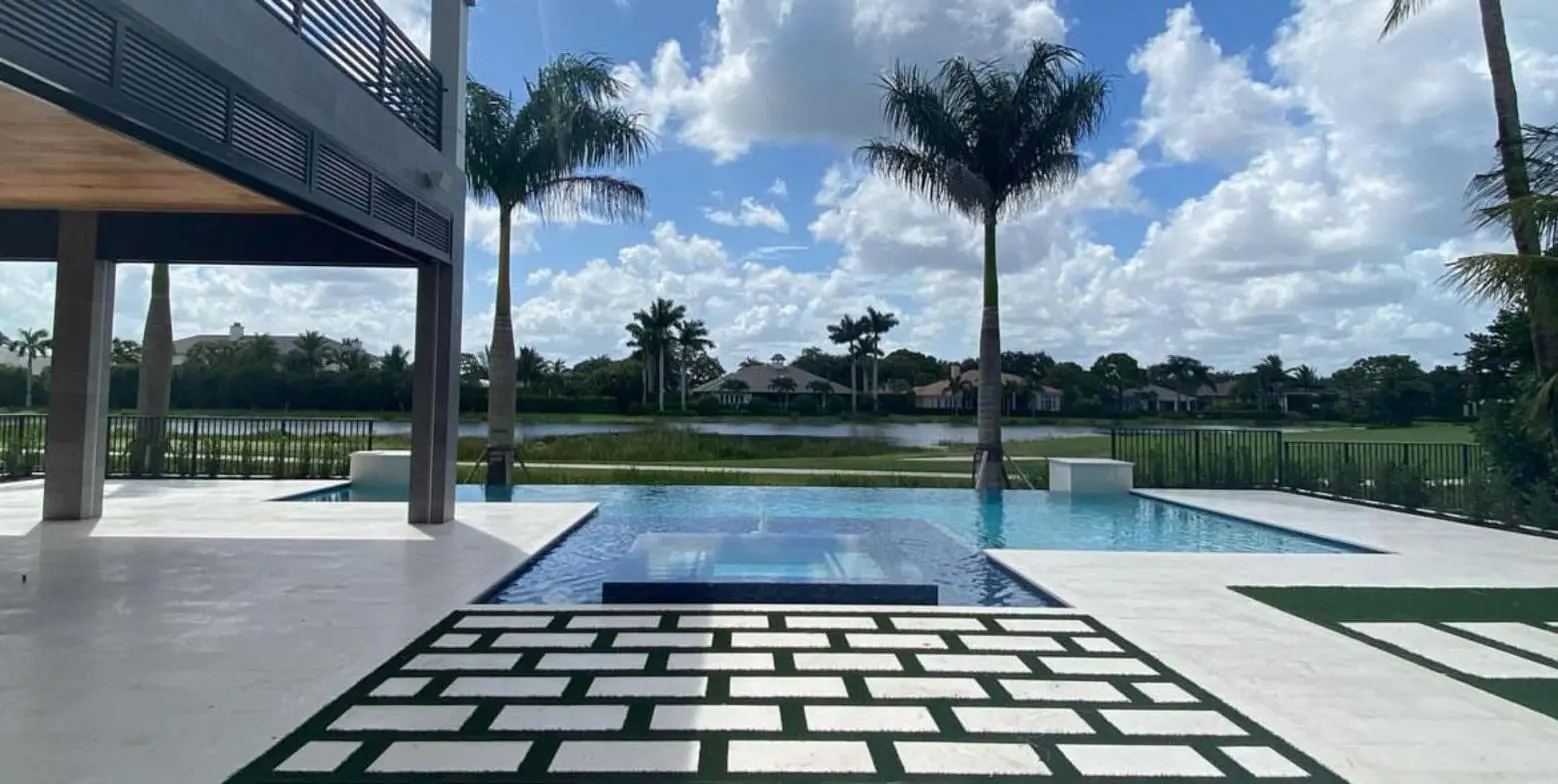 Infinity-edge pool and spa on a travertine deck overlooking a lake and palm trees